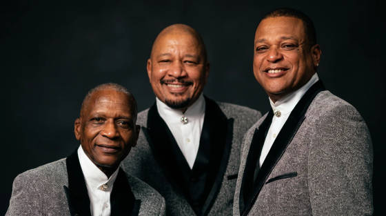 Three men smiling in matching grey suits with black details