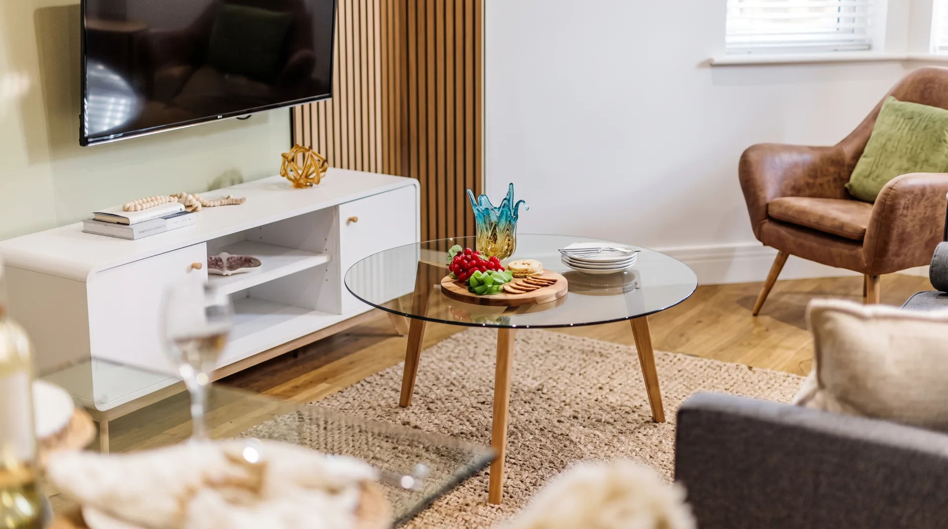 Stylish living area with glass coffee table, fruit platter, TV, and comfortable seating