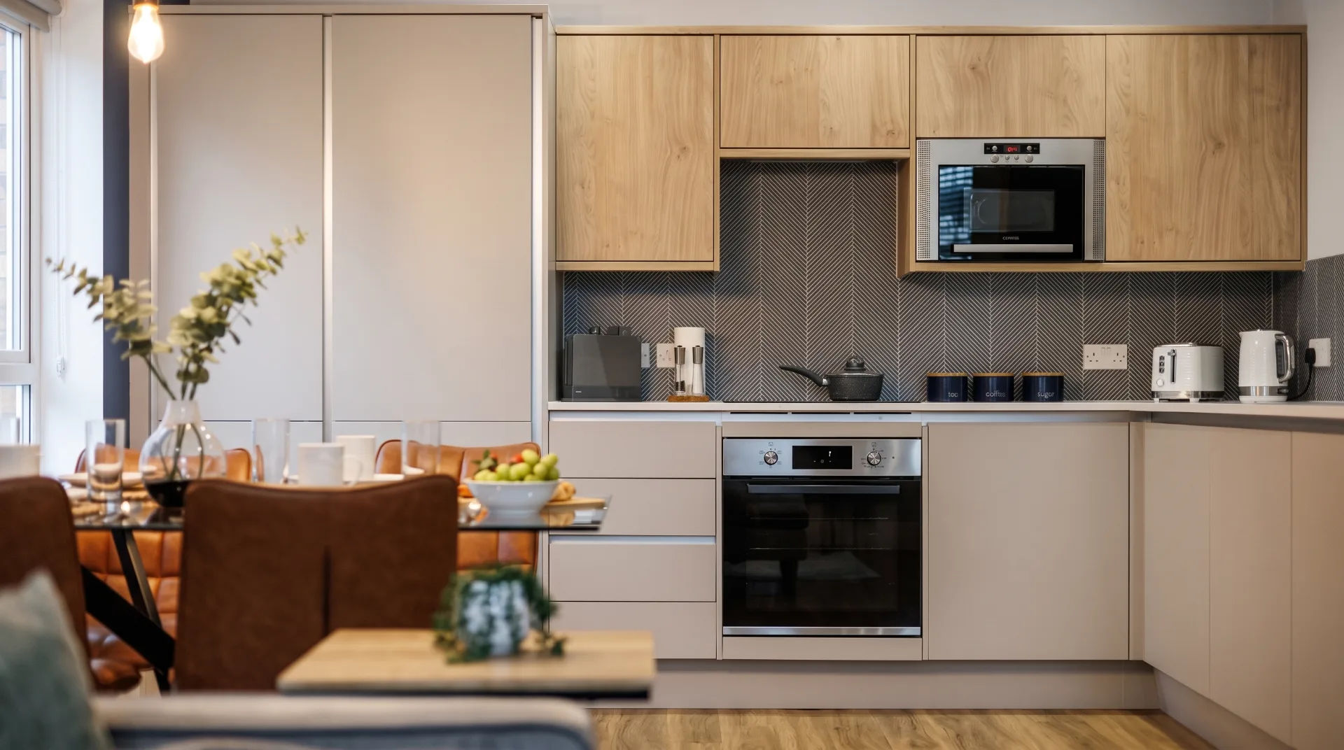 Modern kitchen with wooden cabinets, appliances, and dining area in Tower House Apartments