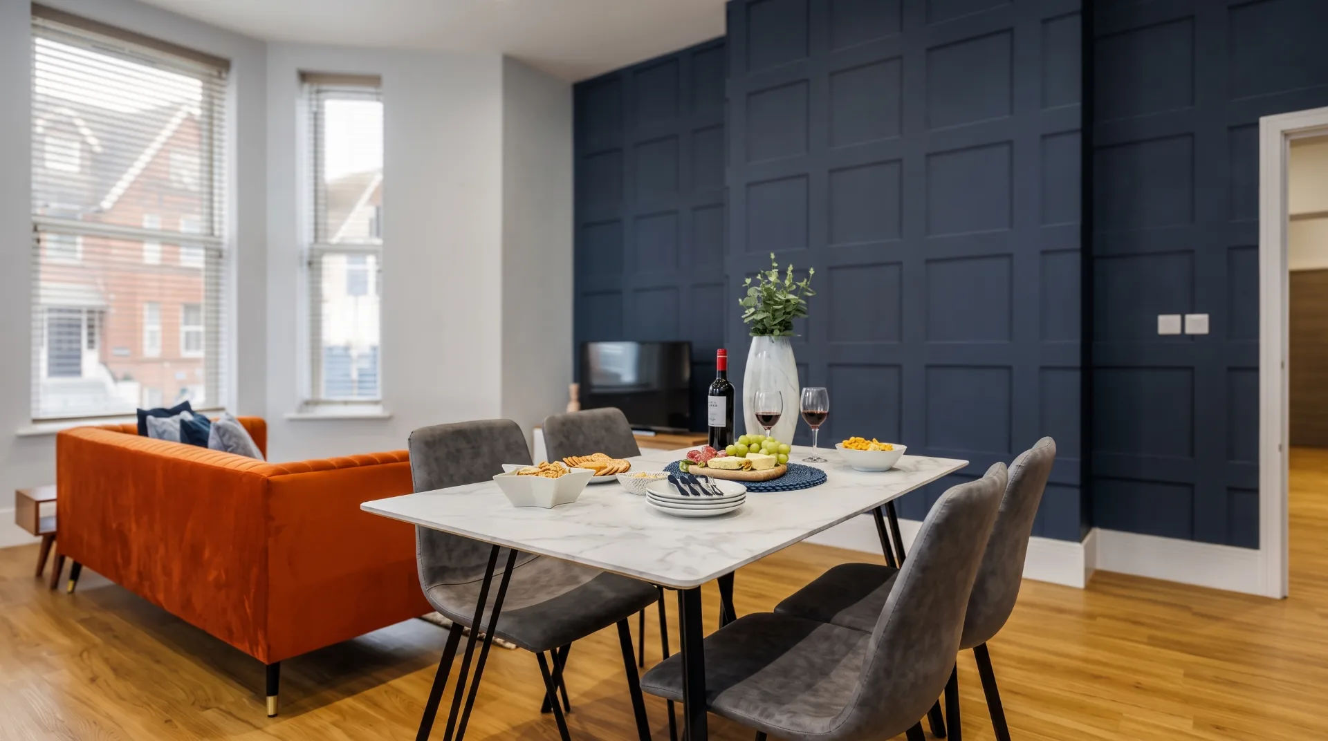 Stylish dining area with a marble table, grey chairs, and an orange sofa in a modern apartment.