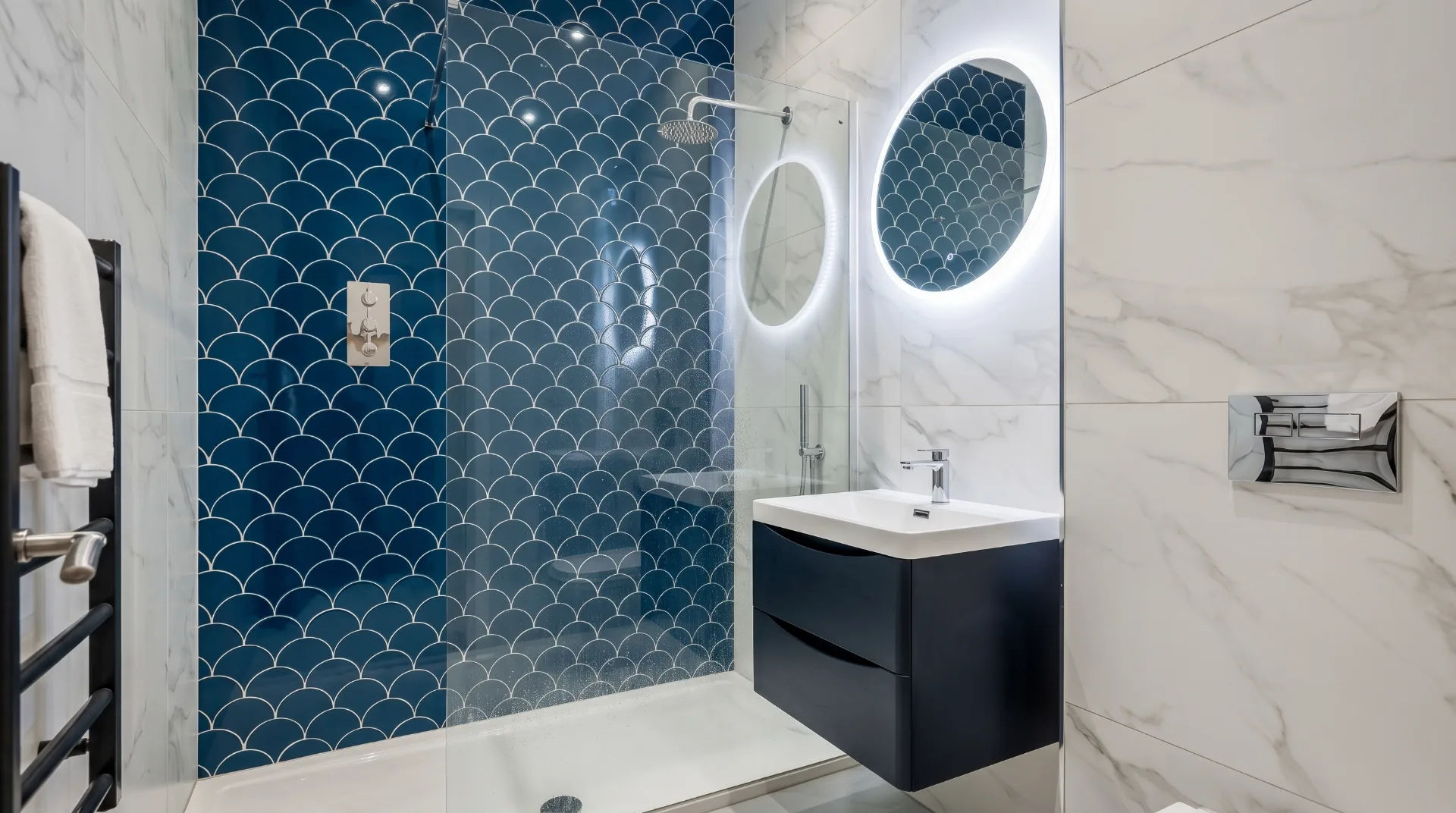 Modern bathroom featuring a blue scalloped tile wall, glass shower, and sleek vanity with a circular mirror.