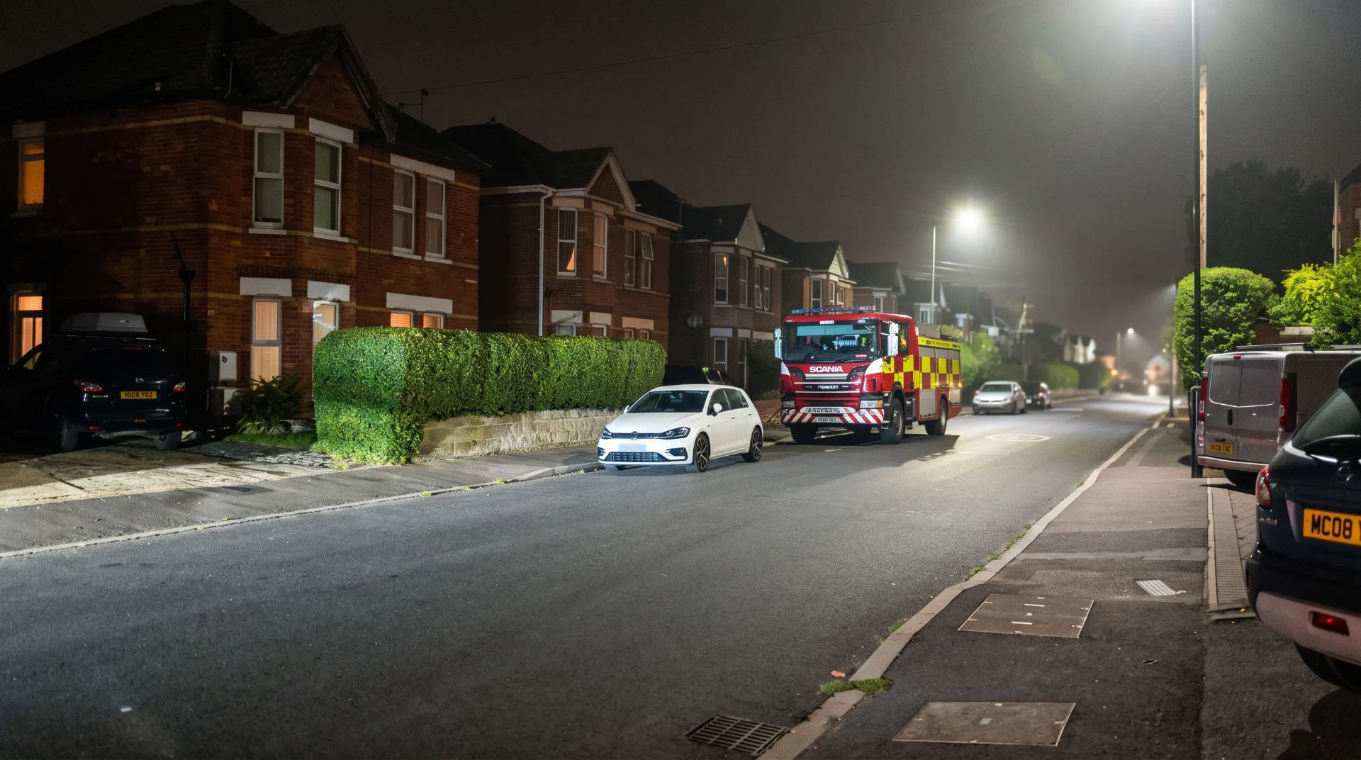 Emergency services vehicle parked on a residential street at night, with houses and streetlights visible