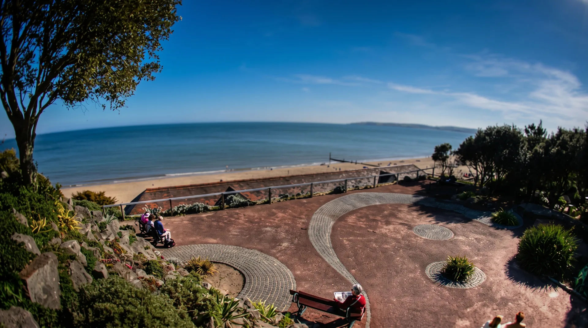 View from a park overlooking the beach, with benches and coastal vegetation in the foreground.