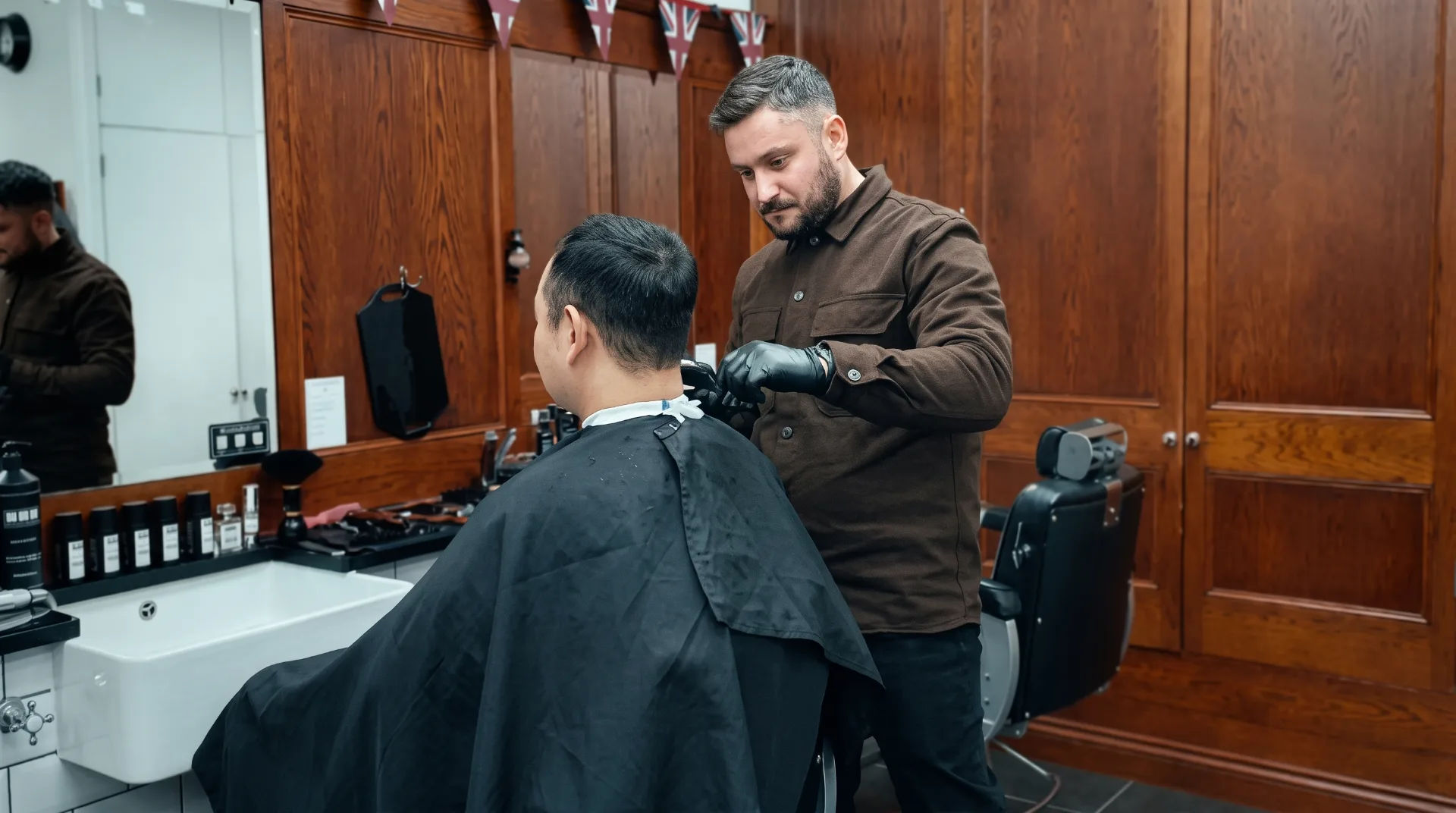 A barber cutting a client's hair in a stylish barbershop with wooden panels and grooming products on display.