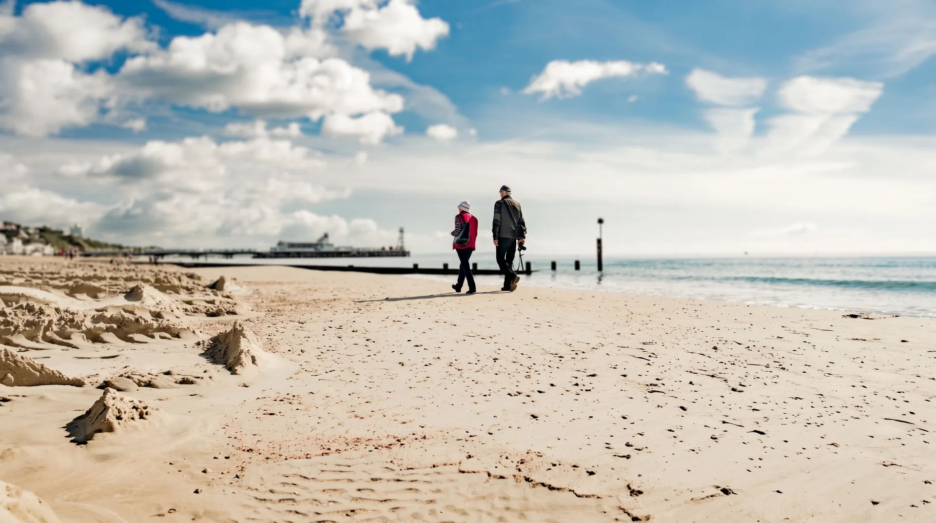 Two people walking along a sandy beach with clouds and sea in the background