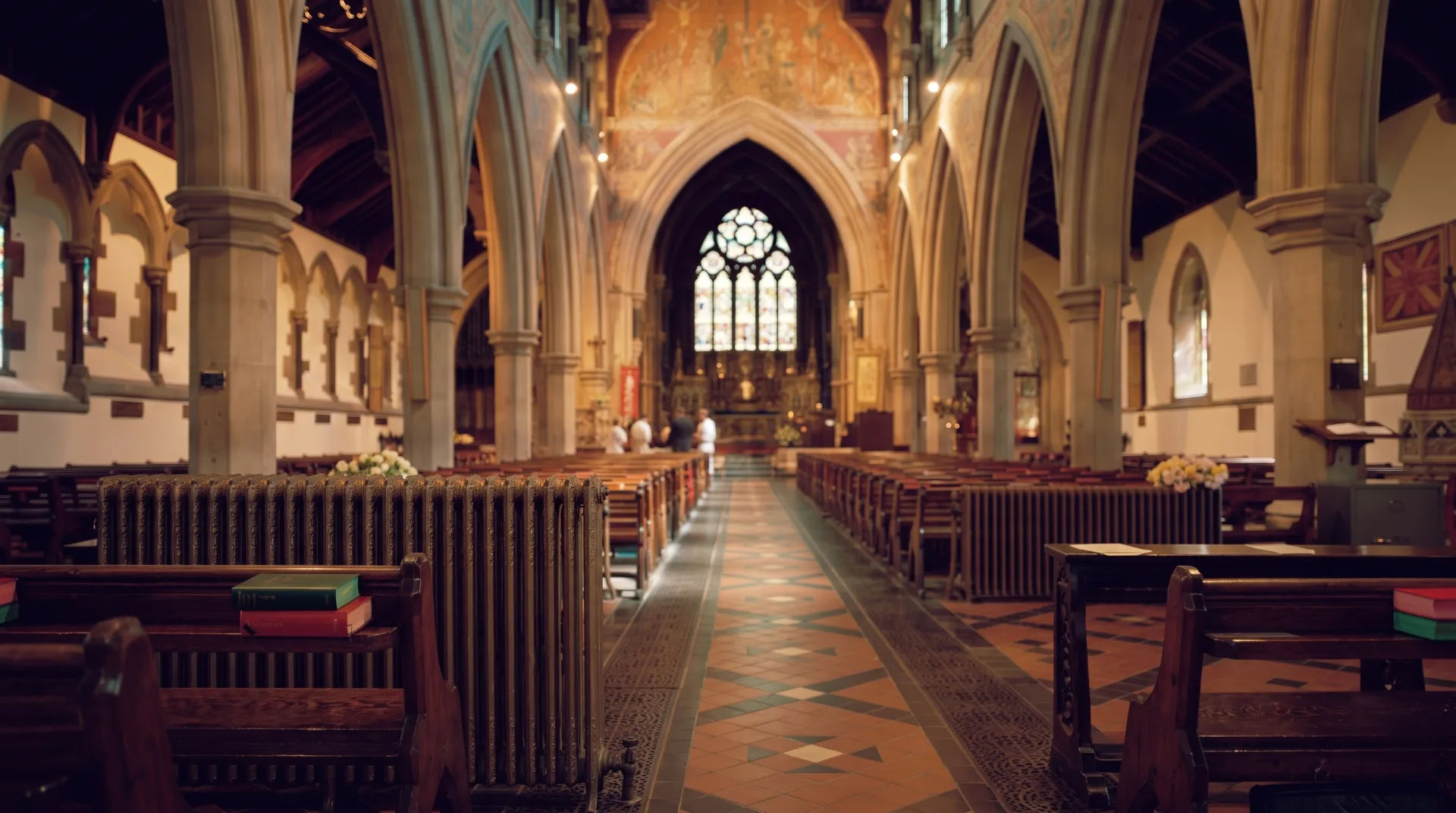 Interior of a church featuring wooden pews, colourful stained glass, and intricate arches