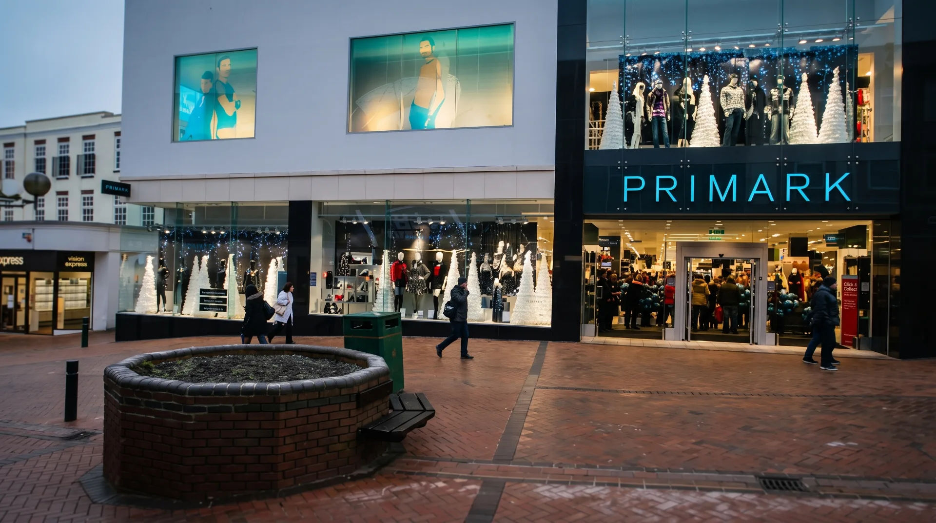 Primark store front with large windows displaying mannequins and festive decorations, shoppers walking by
