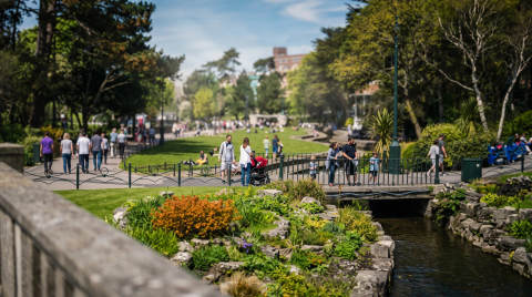 Visitors walking in a green park with flowers and a stream