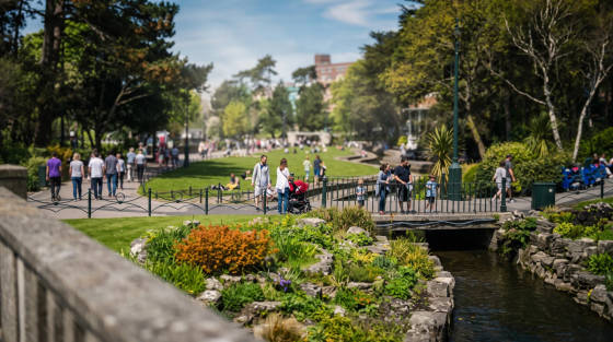 Visitors walking in a green park with flowers and a stream
