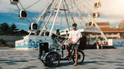 A young man stands beside a rickshaw near the Bournemouth Wheel