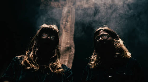 Two people with long hair looking upwards in dim light