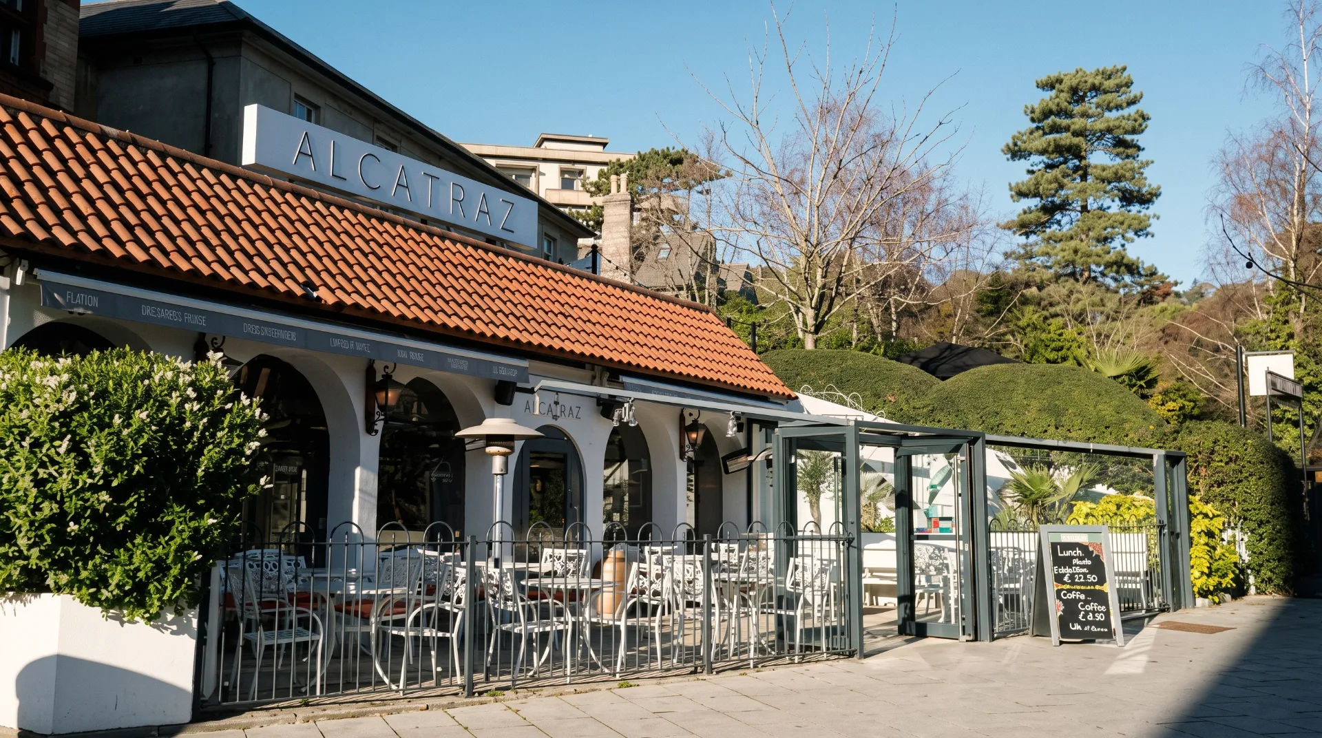 Exterior of Alcatraz restaurant with outdoor seating and a menu board, surrounded by greenery and trees