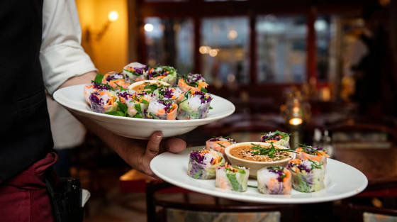 Two plates of spring rolls with a dipping sauce held by a waiter