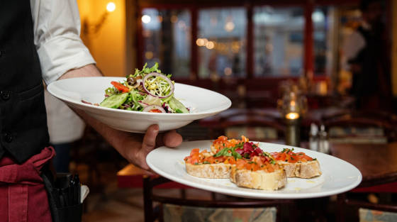 A waiter holding a plate of salad and bruschetta in a restaurant