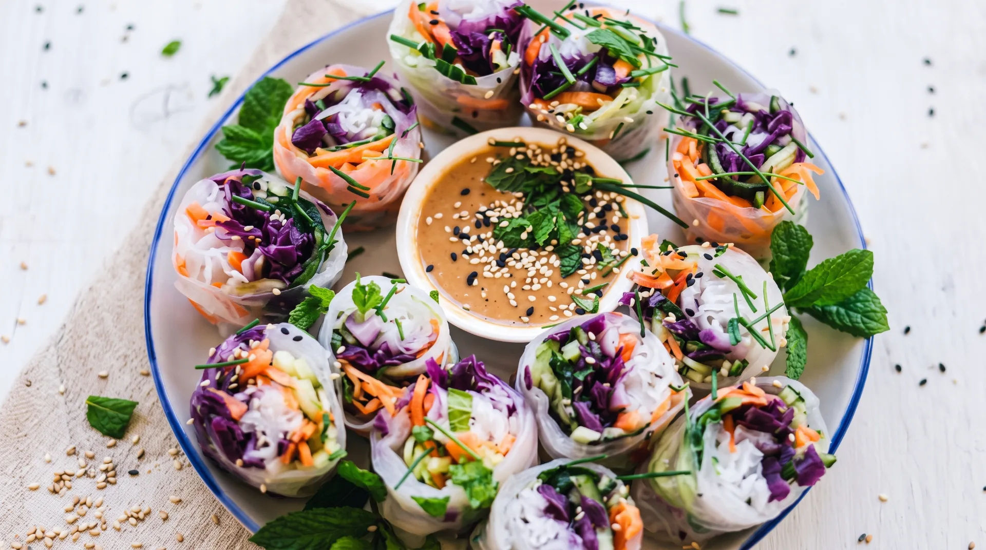 A plate of colourful vegetable spring rolls with a peanut dipping sauce and garnished with mint leaves.
