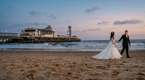 A bride and groom walking hand in hand on the beach near Bournemouth Pier