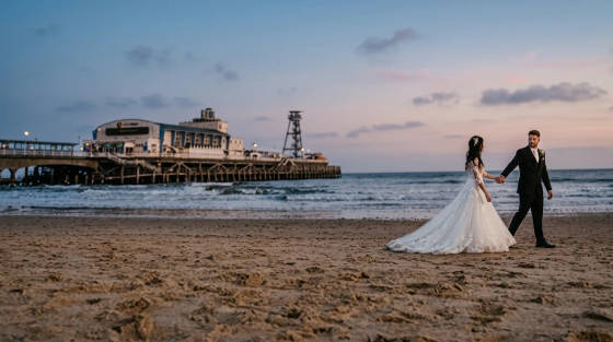 A bride and groom walking hand in hand on the beach near Bournemouth Pier