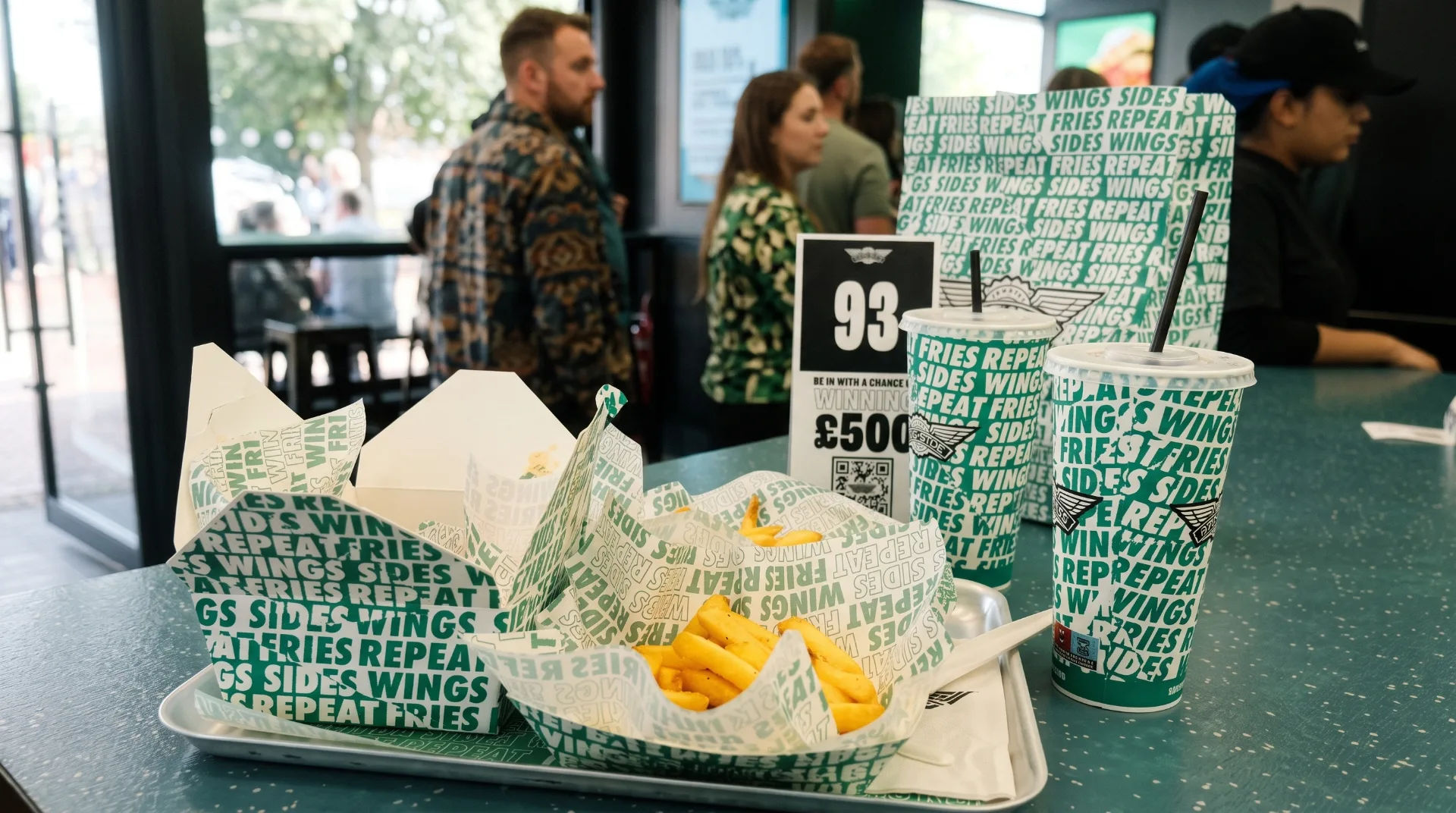Takeaway food containers and drinks on a table in a busy restaurant with people in the background