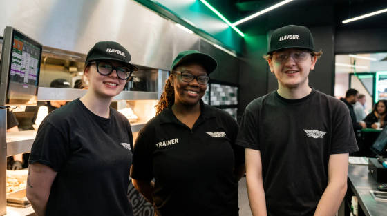 Three staff members in black uniforms and caps standing in a restaurant