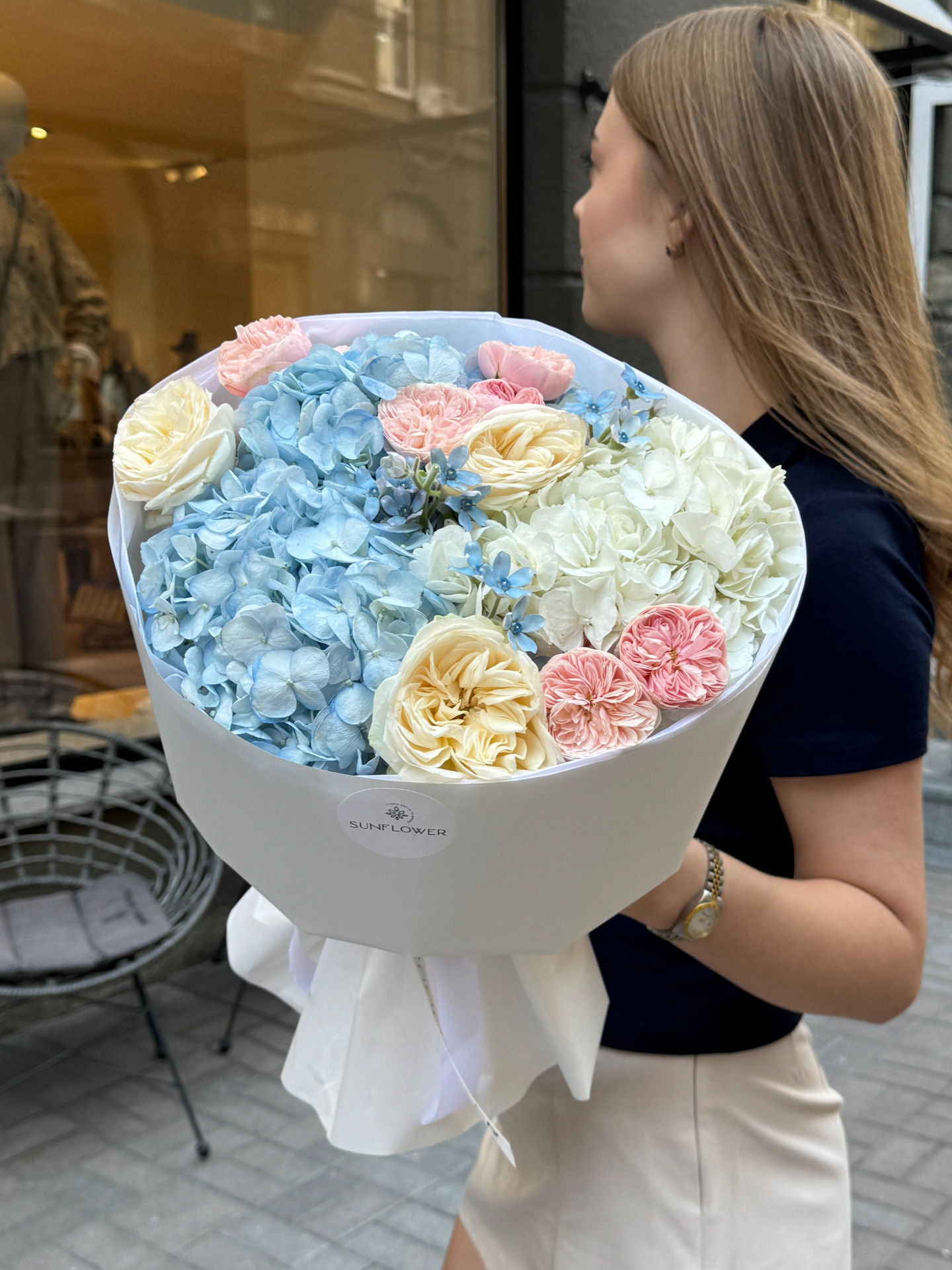 A bouquet of blue and white hydrangeas, cream roses, and soft pink flowers in a light pastel palette.