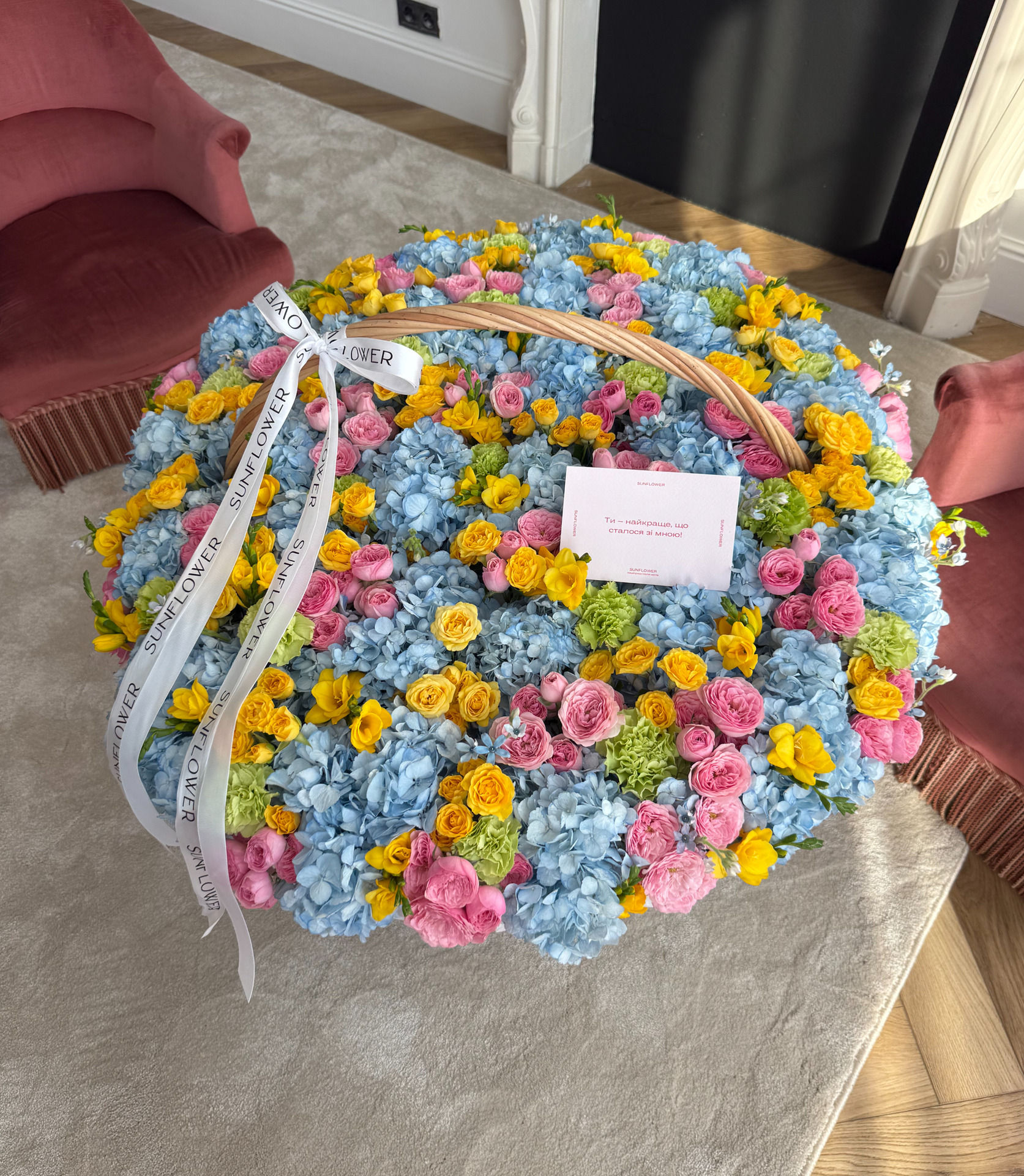 A collection basket with blue hydrangeas, bush roses, and dianthus in bright colors