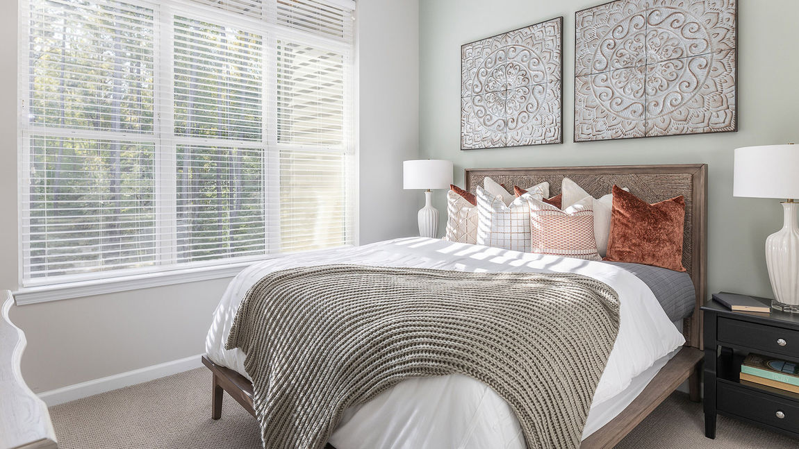 Modern senior apartment bedroom with knitted blankets on a bed and gray lotus-designed metal art pieces on the wall above.
