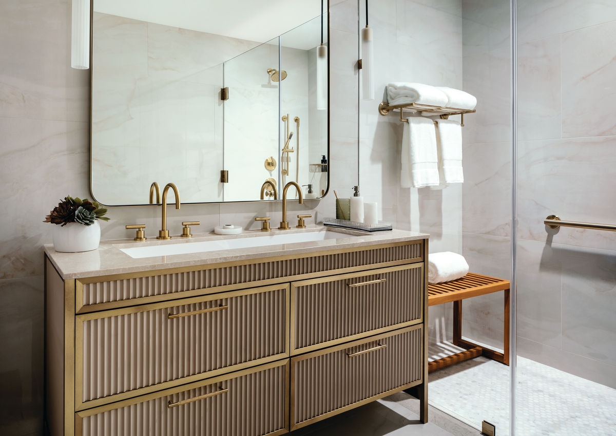 Cathedral Hill apartment bathroom showing double sink, walk in glass door shower and gold fixtures.