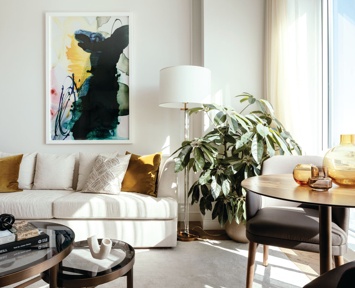 Cathedral Hill living room showcasing white couch, artwork, lamp, leafy green plant, table by the window with bright light.