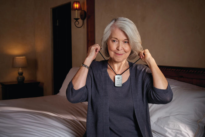 Senior resident sitting on bed putting lively moible device around her neck.