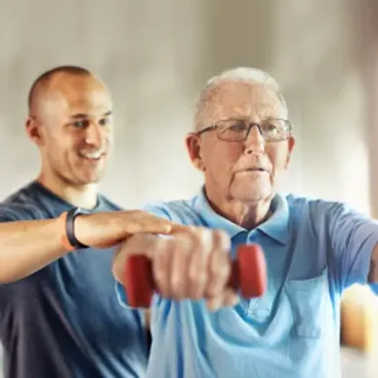 Senior resident working arms out with hand weight with rehab employee assisting.