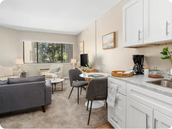 Senior living apartment - showcasing kitchenette with stone counters, a small dining table and seating in living area.