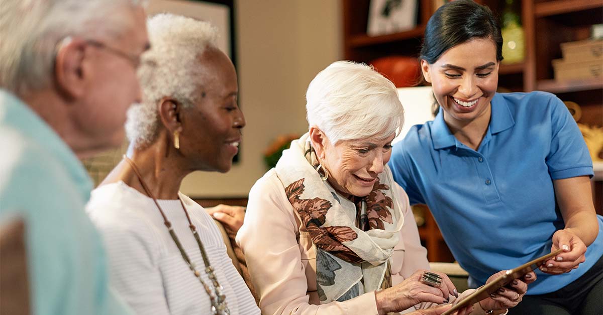 Three Atria Senior Living residents and an Atria employee looking at an iPad together