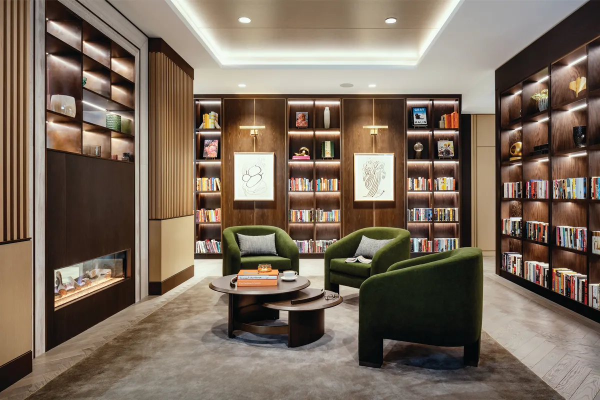 Library at Coterie Cathedral Hill with bookshelves, artwork and three green chairs for reading
