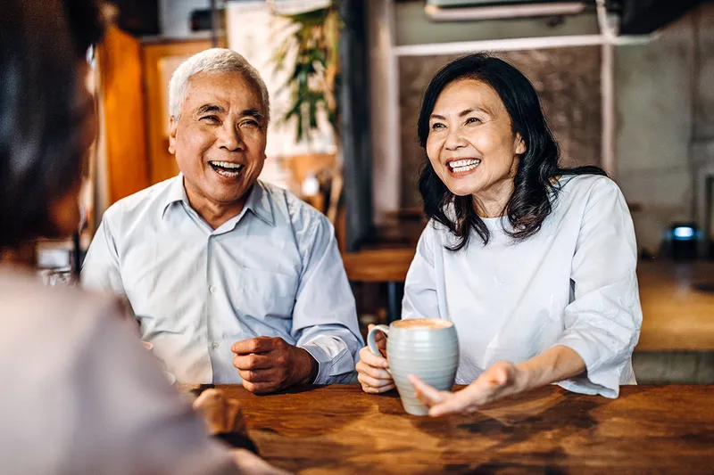 Group of three Asian senior friends sitting and talking in cafe, laughing and having fun