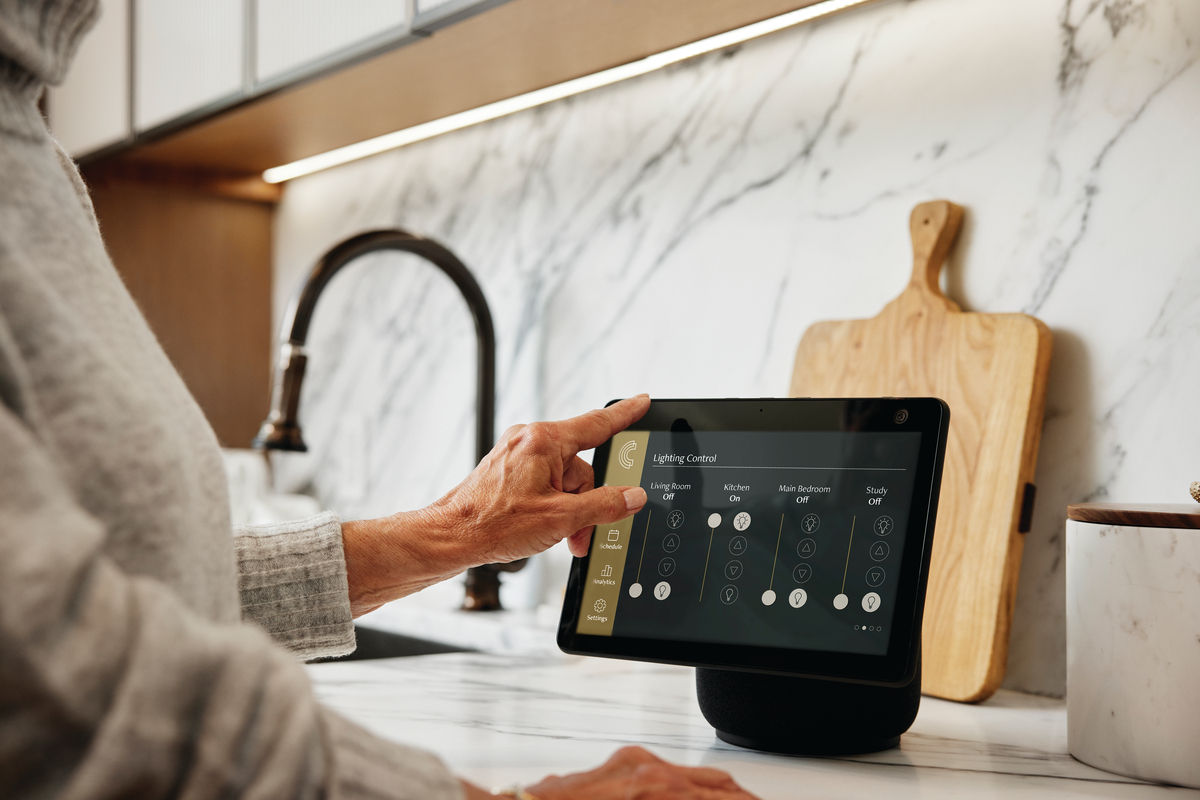 Person using a smart home device on a kitchen counter, adjusting lighting settings. Marble backsplash and wooden cutting board in the background.