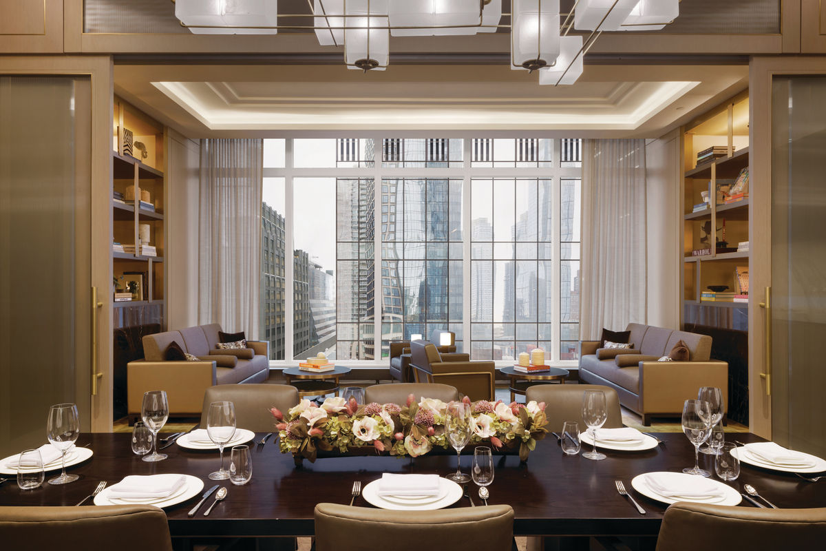 Luxurious dinner table set up with floral center pieve, living area in background and large windows with view of Manhattan