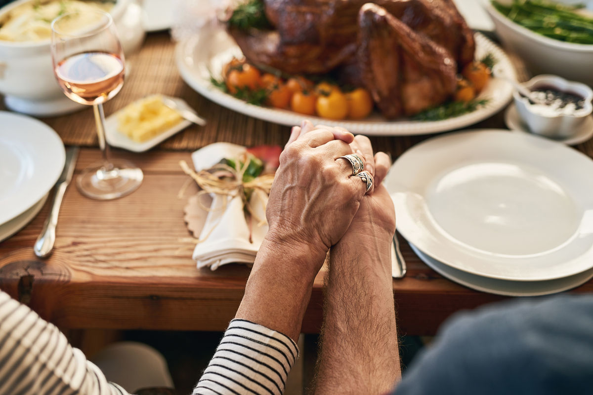 two seniors holding hands at Thanksgiving dinner table with turkey in background on table.