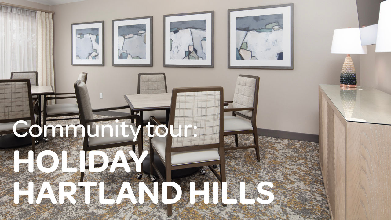 Community room with table and chairs, abstract wall art, lamp and sideboard; text overlay 'Community tour: HOLIDAY HARTLAND HILLS'