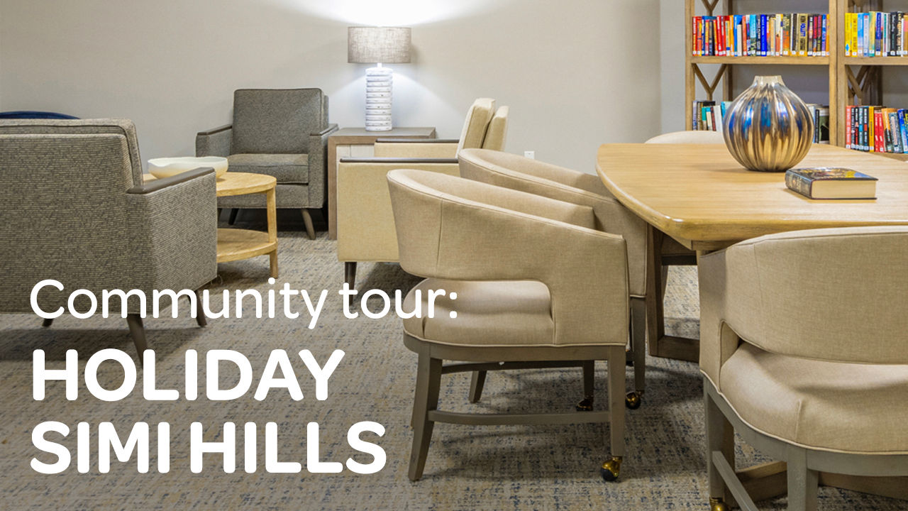 Cozy community room with chairs, a round table, shelves of books, and a lamp. Text reads: "Community tour: Holiday Simi Hills."