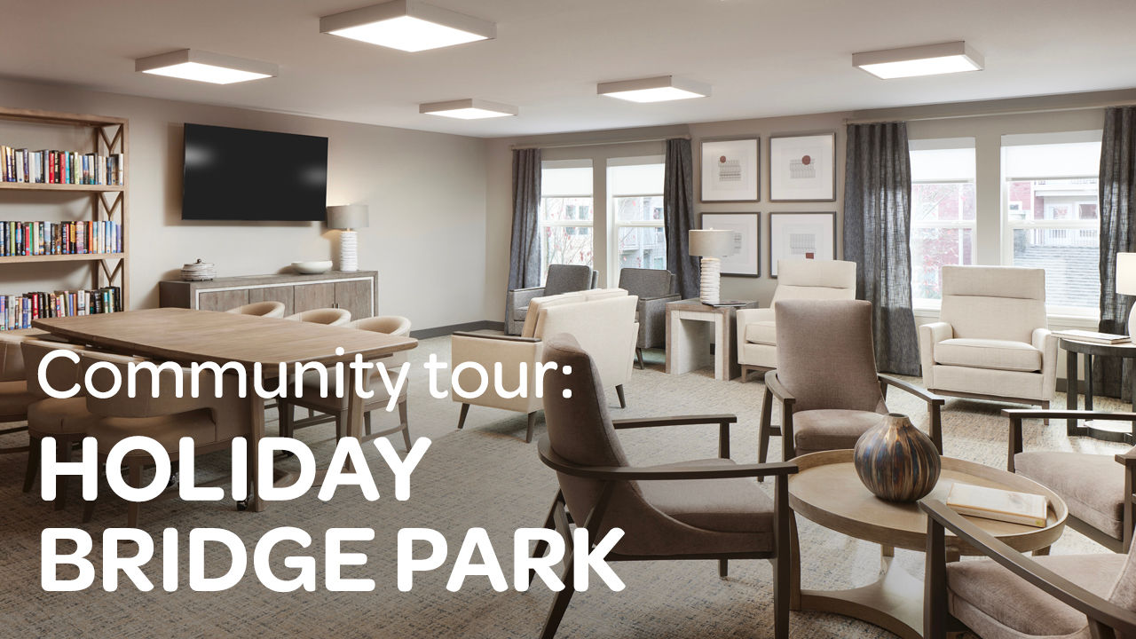 Modern lounge with comfortable seating, a bookshelf, and large windows; caption reads "Community tour: Holiday Bridge Park."