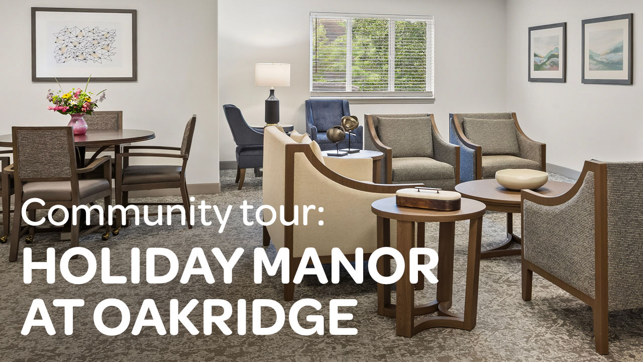 Cozy lounge area at Holiday Manor at Oakridge, with chairs, tables, artwork, and bright window. Text: Community tour: HOLIDAY MANOR AT OAKRIDGE.