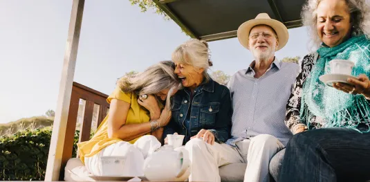 Three senior residents laughing and drinking coffee on Atria Retirement Canada community porch.