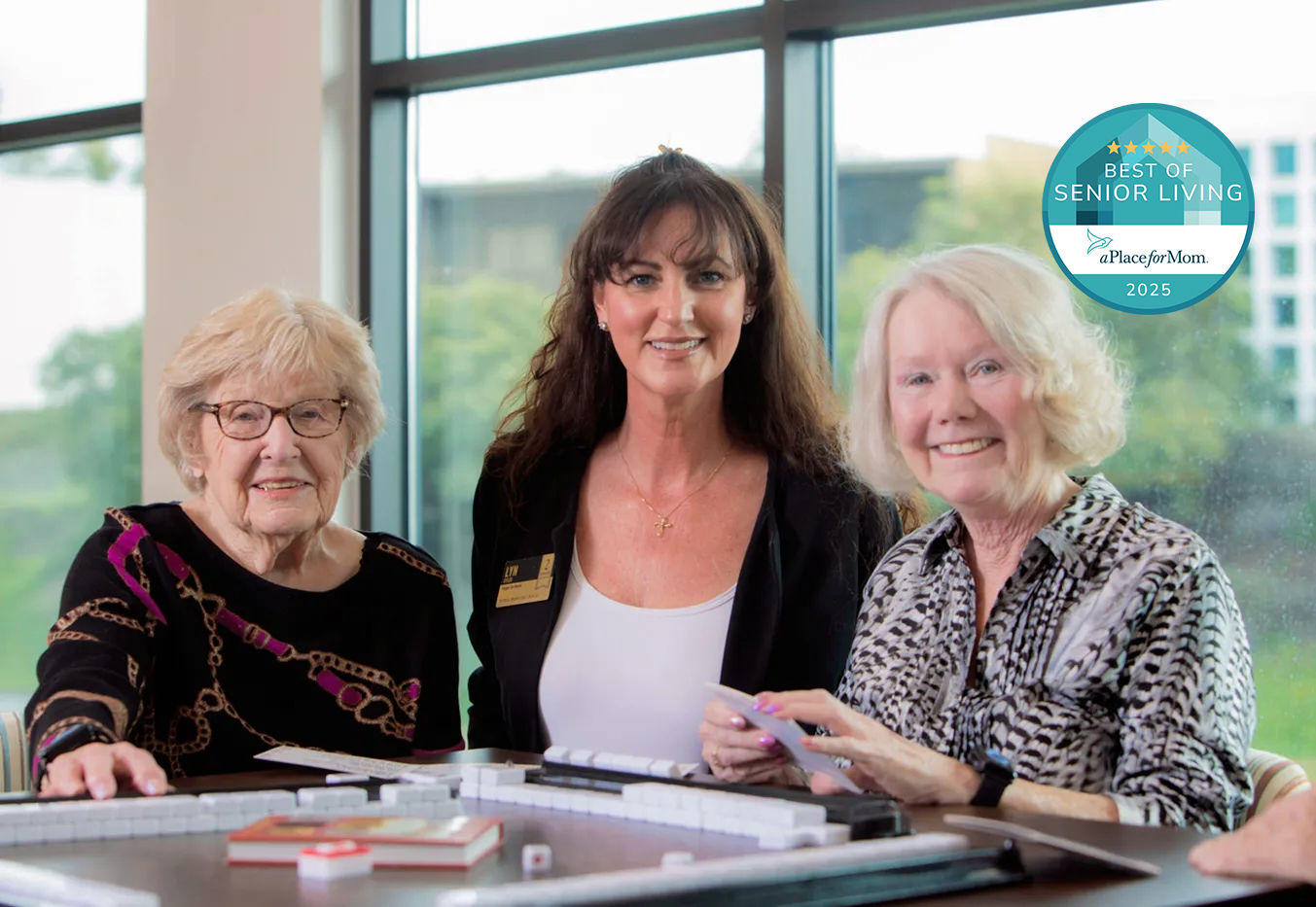 Two Holiday by Atria residents standing next to employee with a Best of Senior Living 2025 badge overlayed