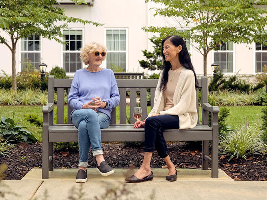 two senior women chatting on a bench together outside