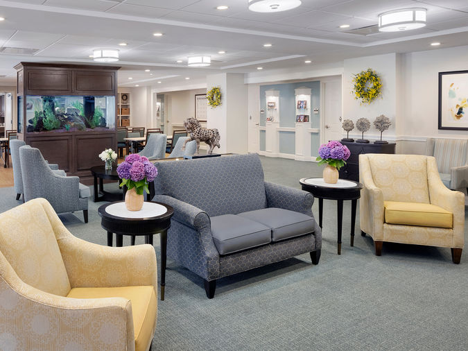 A spacious, elegantly furnished lounge with sofas, armchairs, round tables with purple flowers, and a large fish tank in the background.