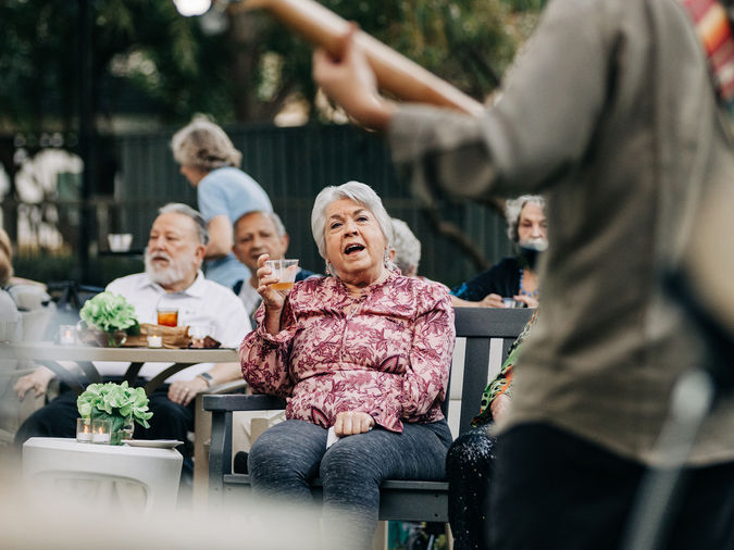 senior woman enjoying an outdoor performance, drinking a glass of wine and singing along