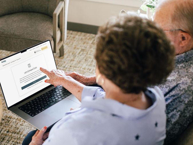 senior couple sitting on a couch together, reviewing their senior living expenses