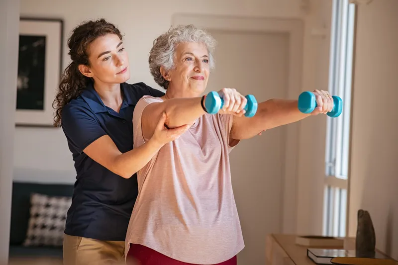 Physical therapy tech assisting a senior woman with handweights.