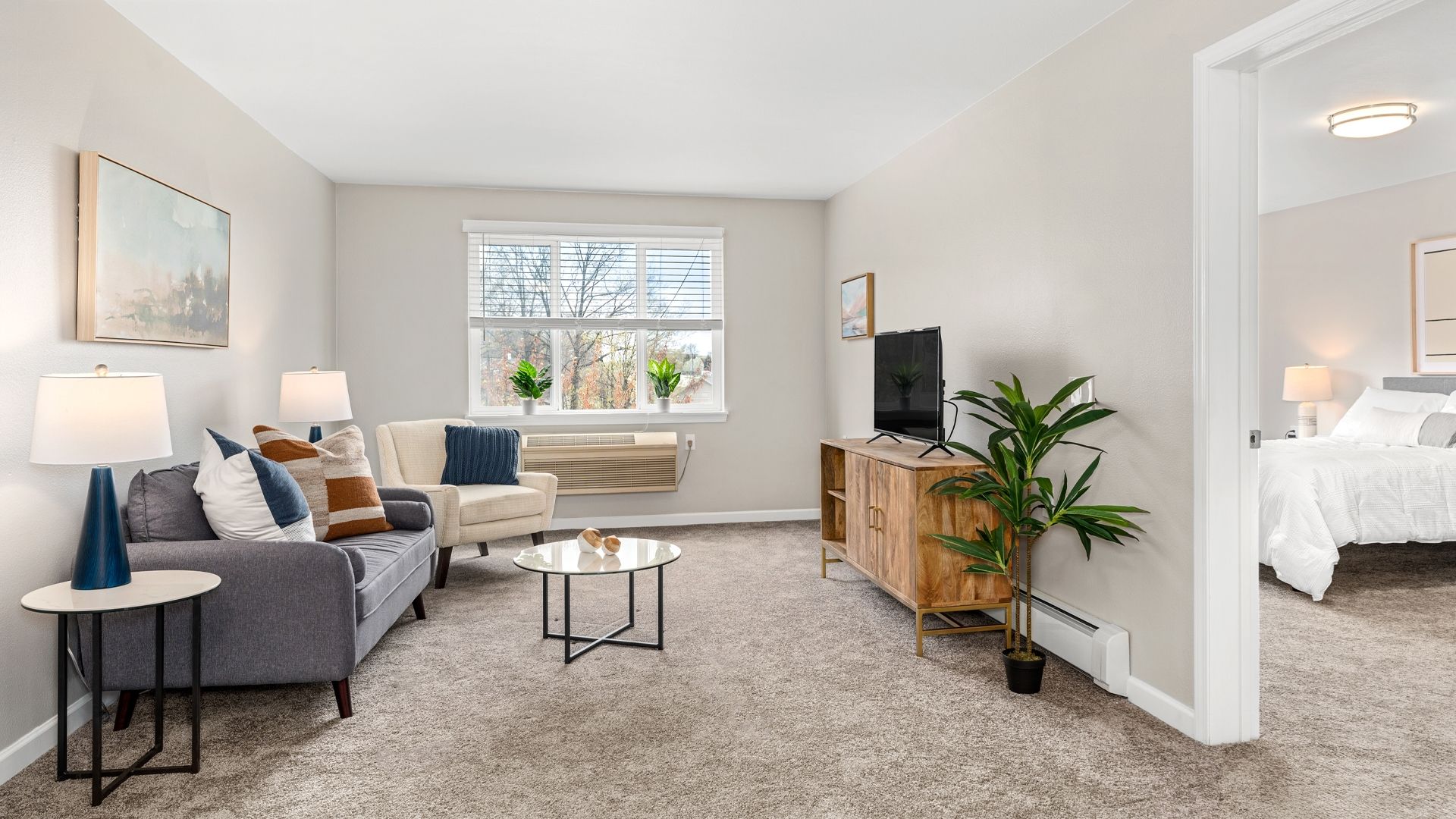 Image of one bedroom apartment. The view is of the living room with a glimpse of the bedroom to the right through an open door.