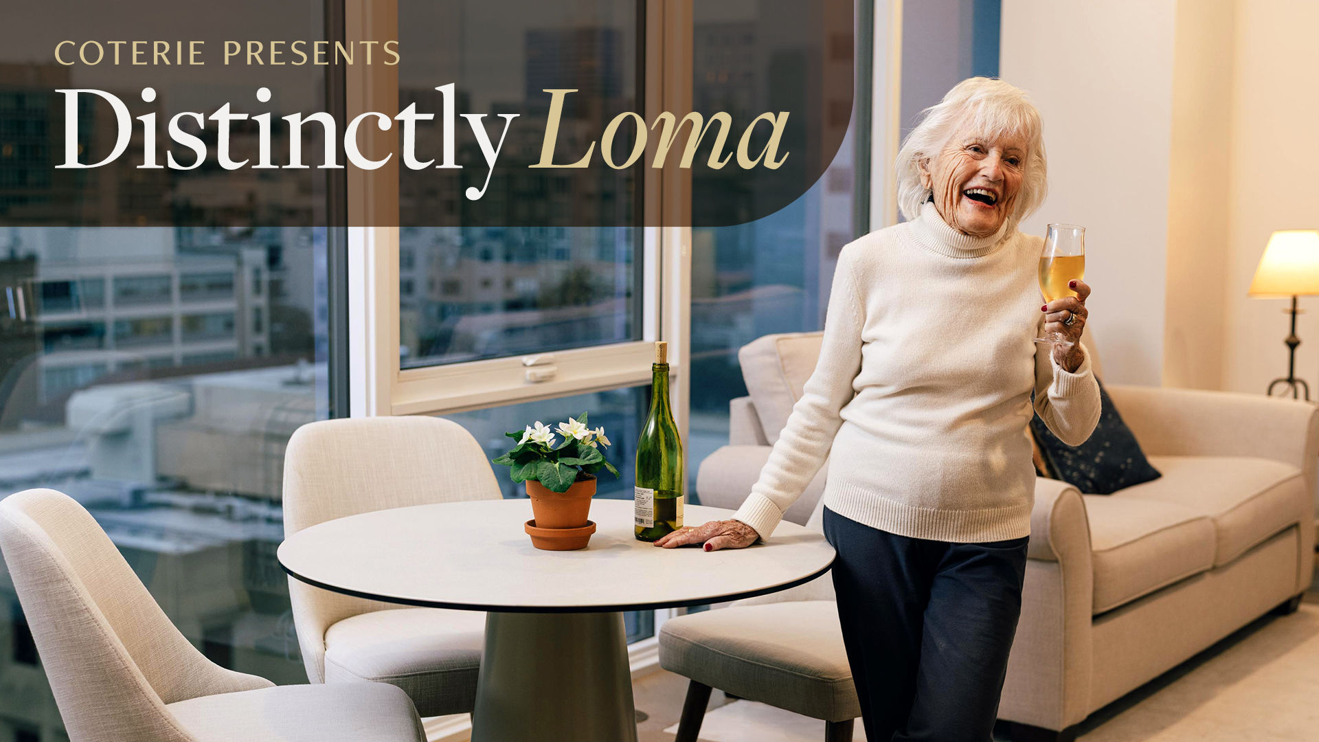 Elderly woman smiling, holding a wine glass in a cozy, upscale apartment with city view, sofa, and a small table with a plant and wine bottle.